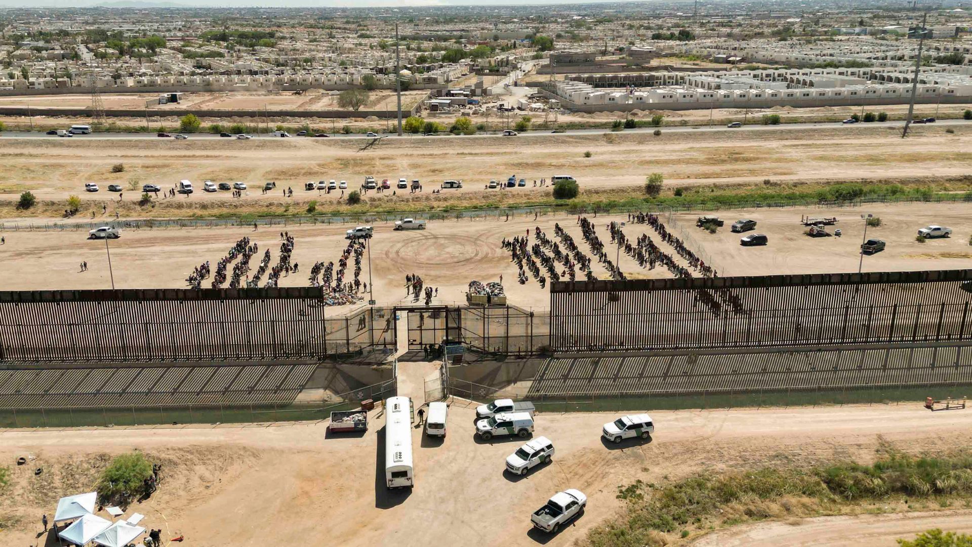 Migrantes mientras esperan junto al muro fronterizo en El Paso, Texas - Foto de referencia: EFE