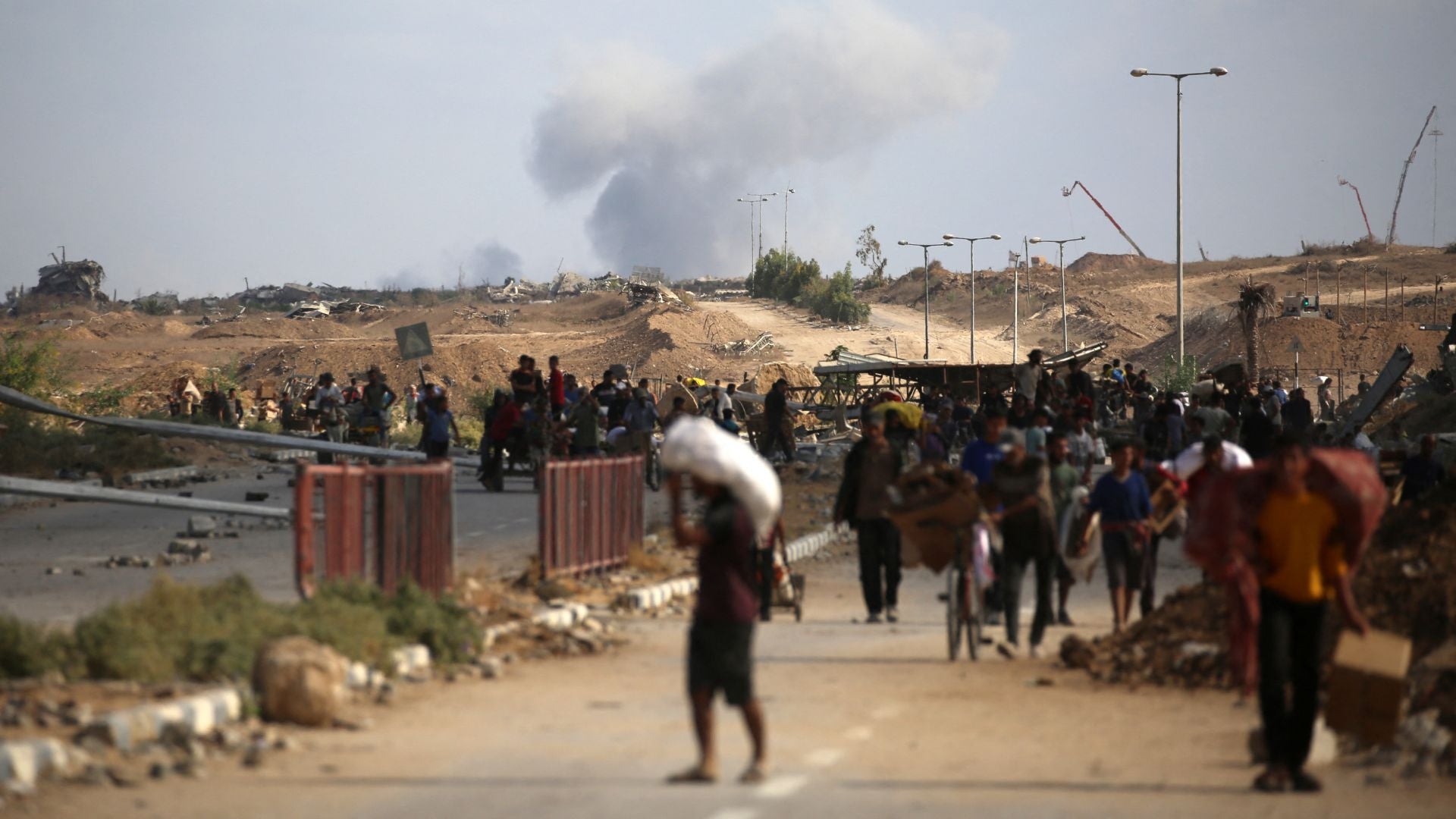 Una columna de humo se eleva al fondo mientras los palestinos regresan de un punto de distribución de alimentos en la franja de Gaza-Foto: AFP
