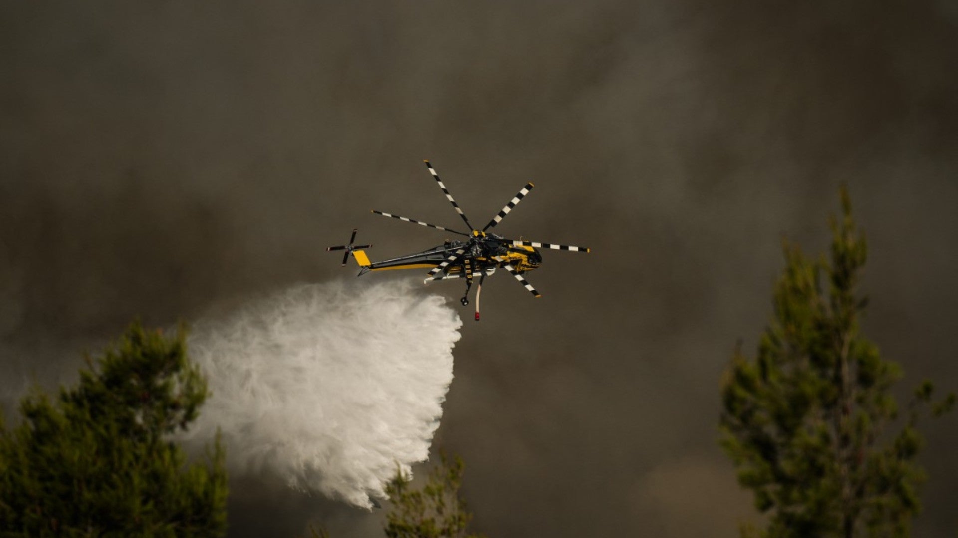 Un helicóptero de extinción de incendios arroja agua sobre una columna de humo de un incendio forestal en Grecia - AFP