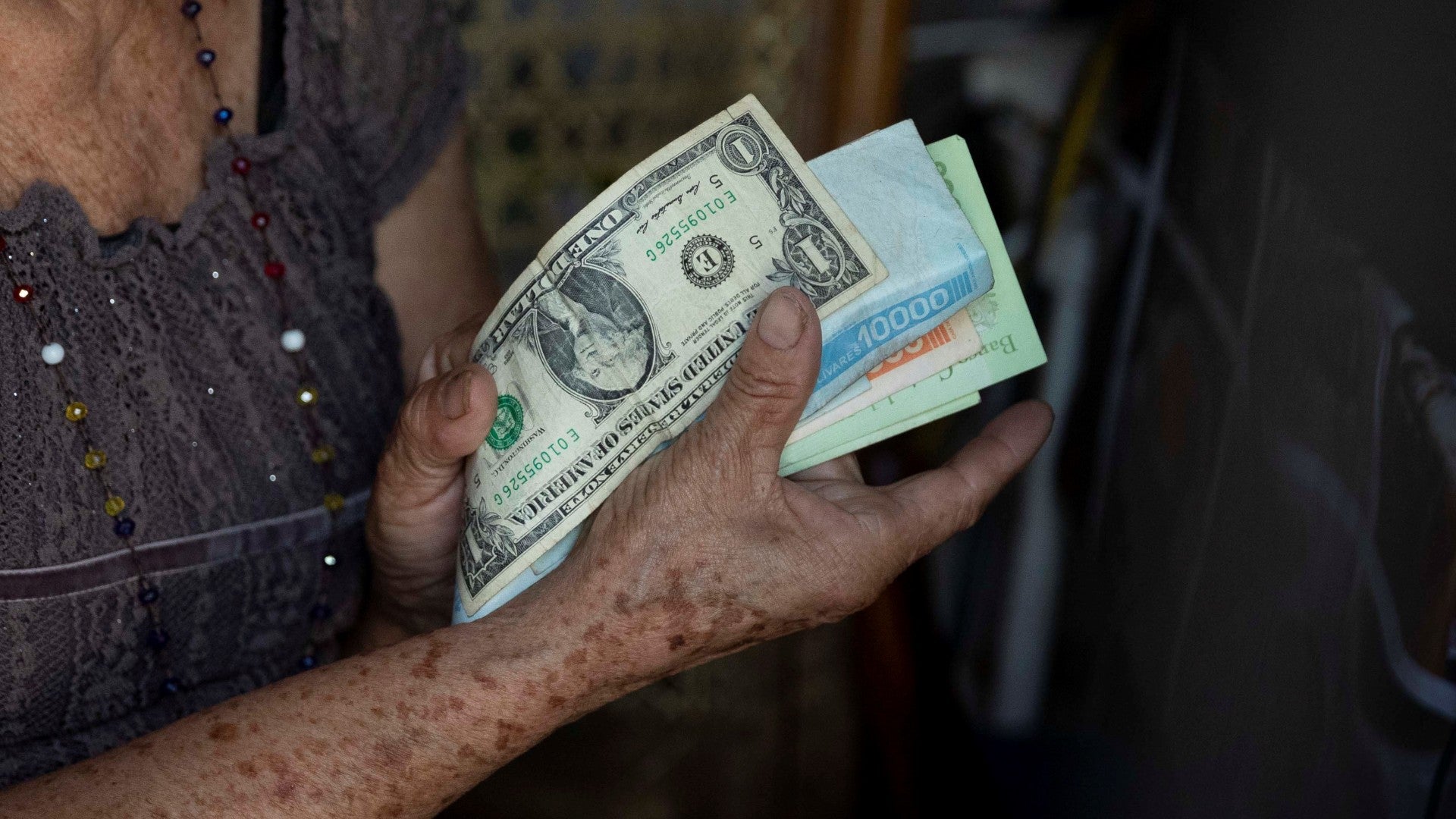 Una adulta mayor sostiene billetes (dólares y bolívares) - Foto: EFE