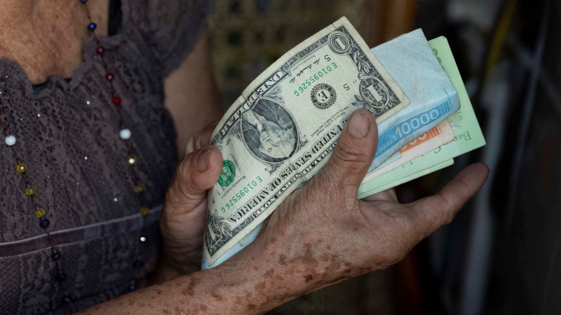 Una mujer de la tercera edad muestra el billete de un dólar y bolívares en Venezuela - Foto de referencia: EFE