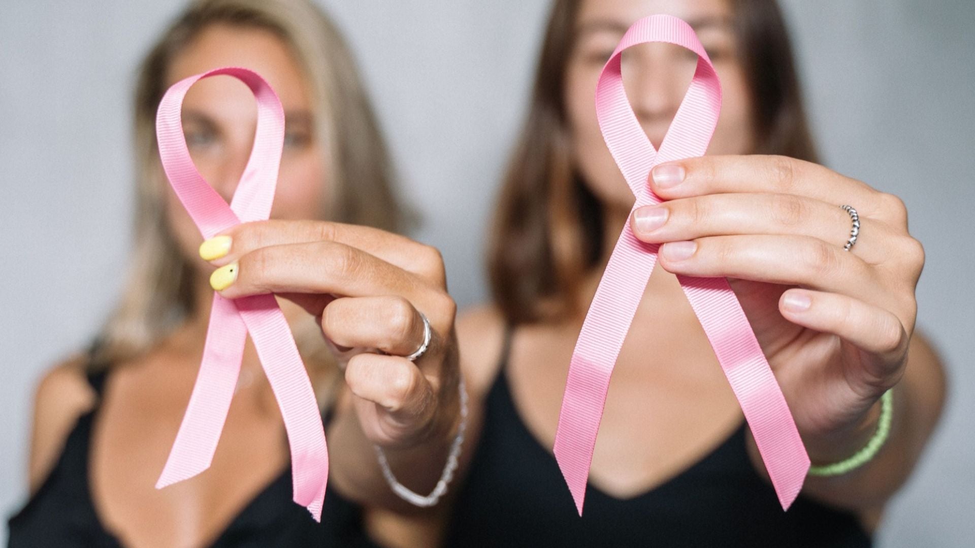 Dos mujeres sosteniendo cintas rosas, simbolizando la concientización y el apoyo al cáncer de mama - Foto de referencia: Pexels