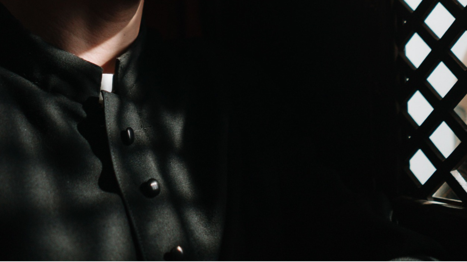 Sacerdote escucha a un penitente en un confesionario tenuemente iluminado - Foto de referencia: Pexels
